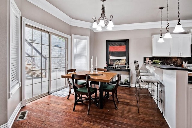 dining room with a notable chandelier, dark wood-type flooring, crown molding, and visible vents