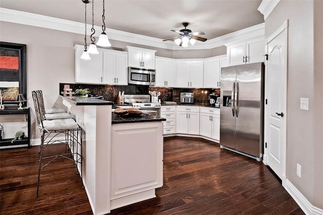 kitchen with a peninsula, stainless steel appliances, dark countertops, a ceiling fan, and dark wood-type flooring