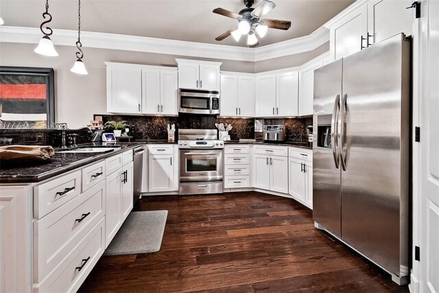 kitchen with crown molding, stainless steel appliances, dark countertops, dark wood-style floors, and a ceiling fan