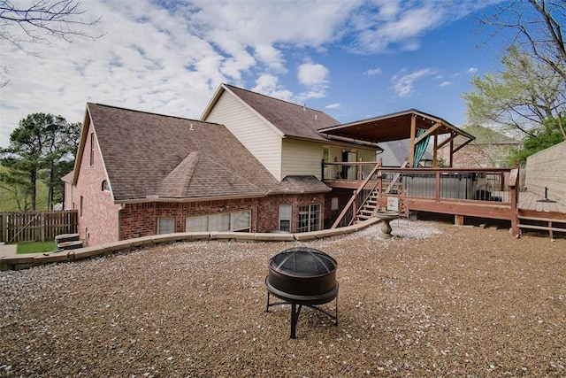 rear view of house featuring roof with shingles, fence, a wooden deck, an outdoor fire pit, and brick siding