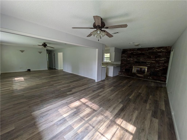 116 Stegall Rd, Clarksville, AR 72830 - unfurnished living room with a ceiling fan, dark wood-style floors, a brick fireplace, and a textured ceiling