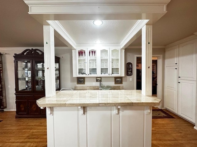 5121 E State Highway 22, Paris, AR 72855 - kitchen with a breakfast bar area, wood finished floors, glass insert cabinets, white cabinets, and ornamental molding