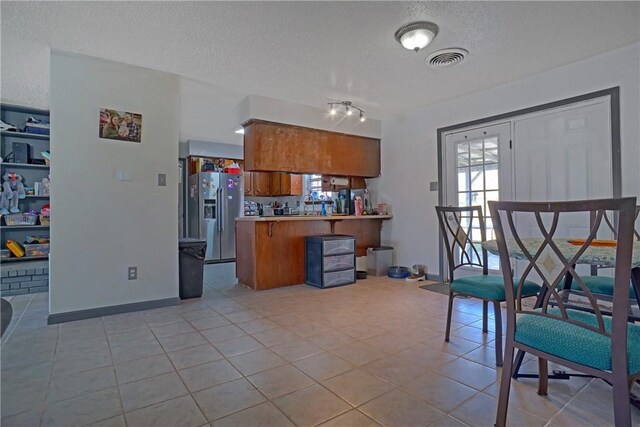 kitchen with stainless steel fridge with ice dispenser, visible vents, a peninsula, a textured ceiling, and brown cabinets