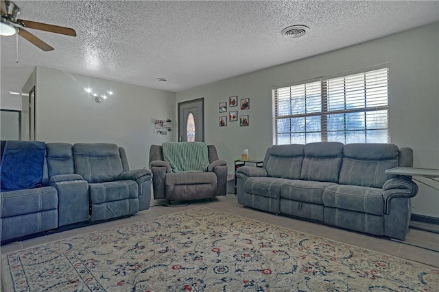 living room featuring tile patterned floors, visible vents, a textured ceiling, and a ceiling fan