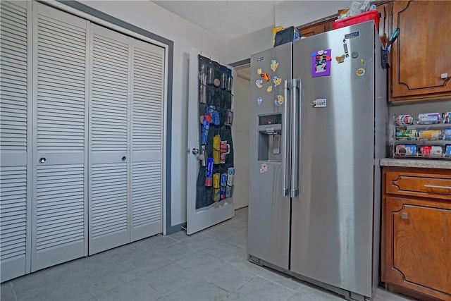 kitchen with light tile patterned floors, light countertops, brown cabinetry, and stainless steel fridge