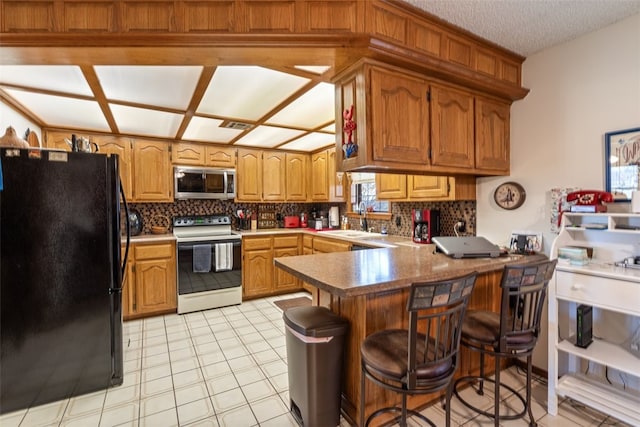 kitchen featuring backsplash, freestanding refrigerator, a peninsula, white range with electric stovetop, and stainless steel microwave