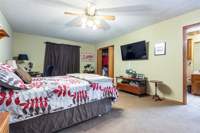 bedroom with a textured ceiling, a ceiling fan, ensuite bath, carpet floors, and a spacious closet
