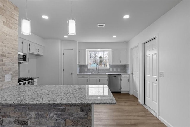 kitchen with white cabinets, stainless steel appliances, visible vents, a sink, and a peninsula