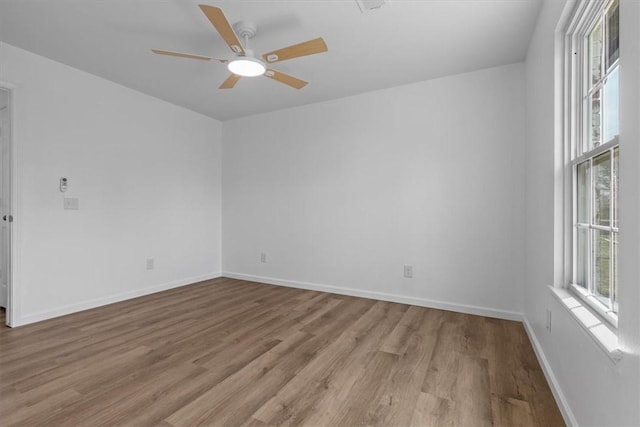 empty room featuring light wood-type flooring, a ceiling fan, and baseboards