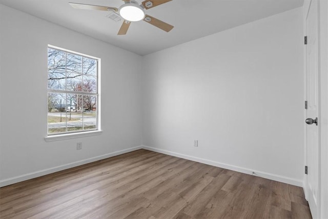 spare room with wood finished floors, a healthy amount of sunlight, a ceiling fan, and baseboards