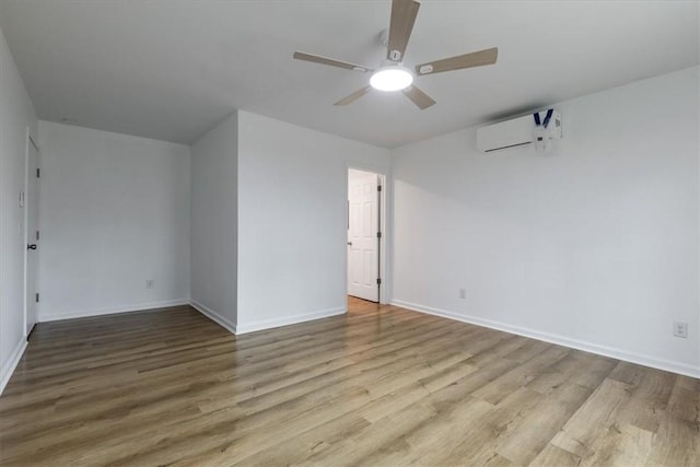 spare room featuring a wall mounted air conditioner, a ceiling fan, baseboards, and wood finished floors