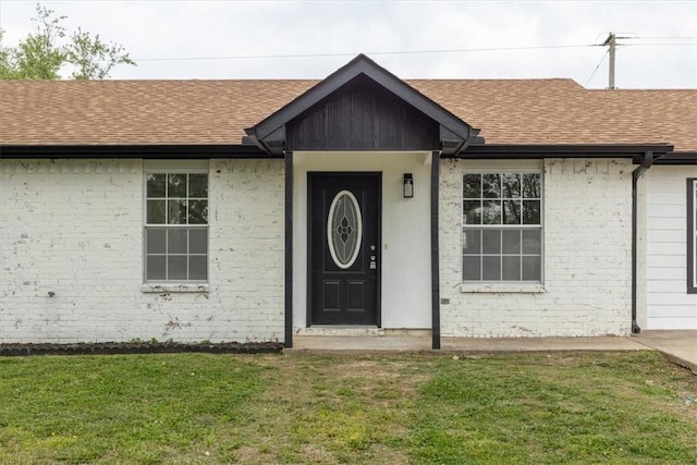 entrance to property featuring a lawn, brick siding, and roof with shingles