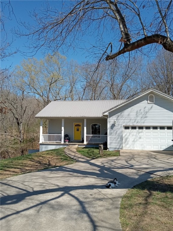 view of front facade featuring an attached garage, metal roof, concrete driveway, and a porch