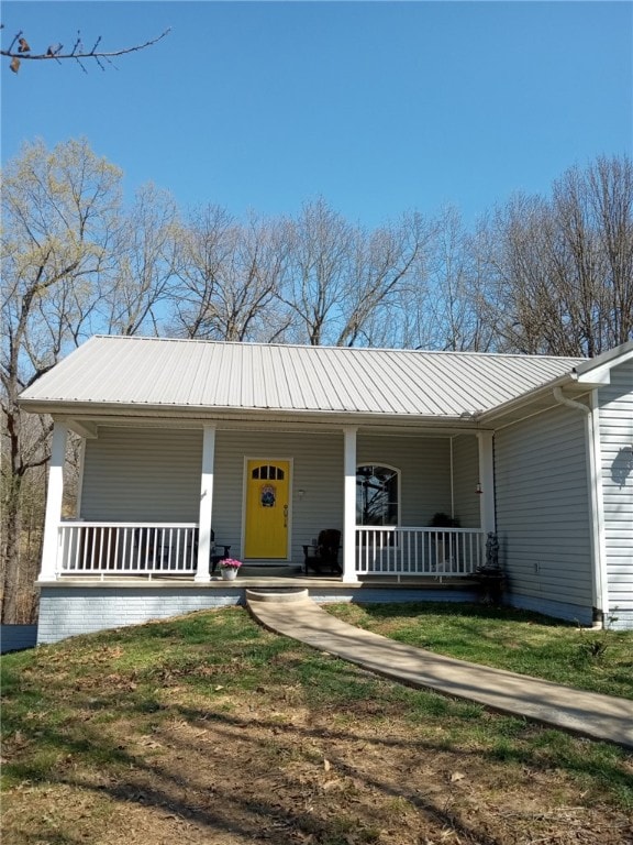 ranch-style home featuring covered porch, a front yard, and metal roof