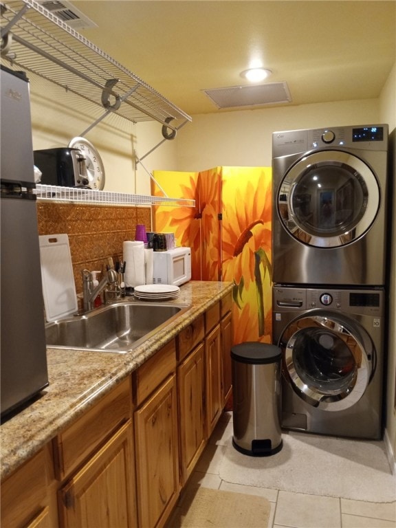 laundry area featuring attic access, light tile patterned floors, stacked washing maching and dryer, a sink, and laundry area