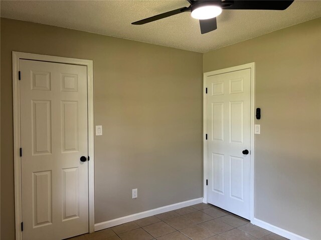 tiled empty room with ceiling fan, baseboards, and a textured ceiling