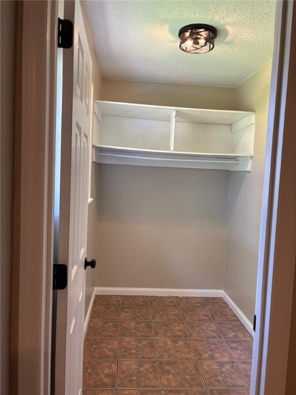 clothes washing area with baseboards, a textured ceiling, and dark tile patterned flooring