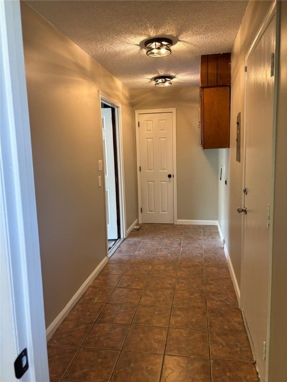 hall featuring a textured ceiling, dark tile patterned flooring, and baseboards