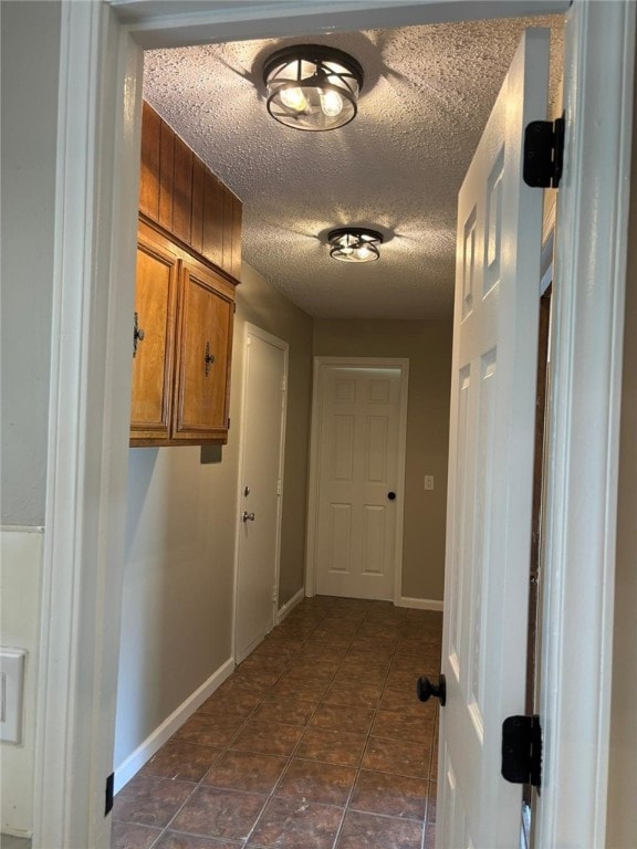 corridor with a textured ceiling, baseboards, and dark tile patterned flooring