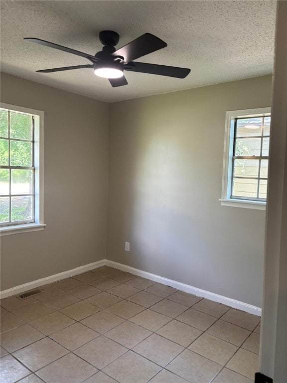 unfurnished room featuring a ceiling fan, plenty of natural light, a textured ceiling, light tile patterned floors, and baseboards