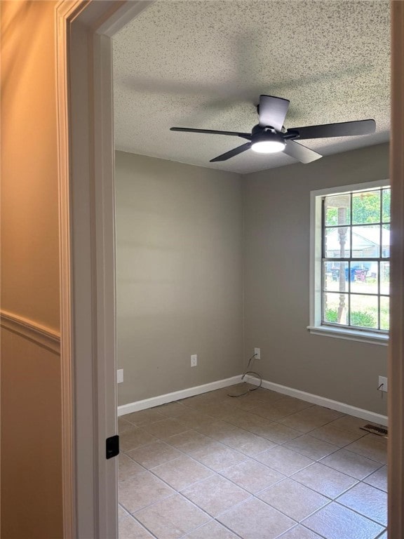unfurnished room with light tile patterned floors, a ceiling fan, baseboards, and a textured ceiling