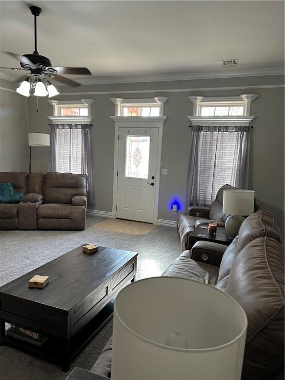 living room featuring baseboards, visible vents, ornamental molding, and a ceiling fan