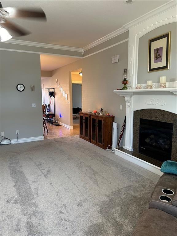 living area with a fireplace, crown molding, ceiling fan, and carpet