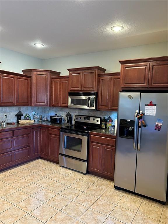 kitchen featuring tasteful backsplash, appliances with stainless steel finishes, a textured ceiling, light tile patterned floors, and dark countertops