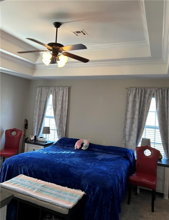 bedroom featuring crown molding, a raised ceiling, carpet floors, visible vents, and a ceiling fan