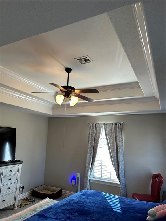 bedroom featuring baseboards, a tray ceiling, visible vents, and crown molding