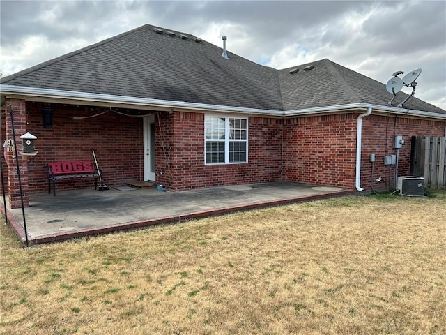 back of property featuring a shingled roof, a patio area, brick siding, and a yard
