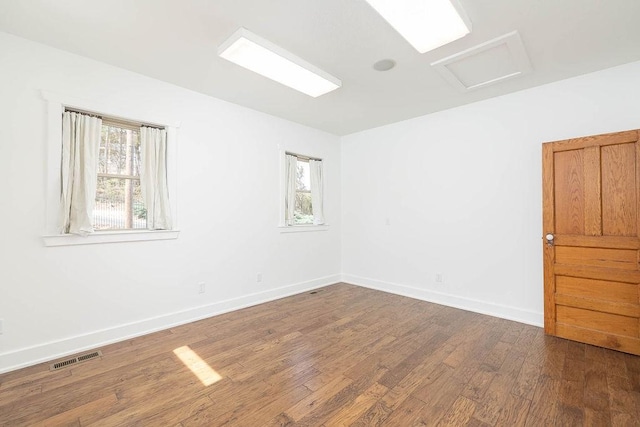 spare room featuring visible vents, attic access, wood finished floors, and a wealth of natural light