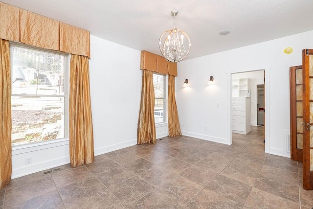 spare room featuring baseboards, visible vents, stone finish flooring, and a chandelier