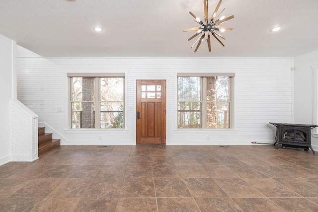 unfurnished living room featuring wooden walls, a wood stove, stairs, recessed lighting, and baseboards