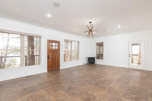 unfurnished living room with an inviting chandelier, a wood stove, baseboards, stone finish flooring, and visible vents