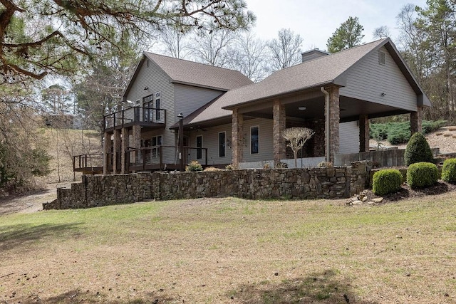 exterior space featuring a shingled roof, a chimney, a front lawn, and a balcony
