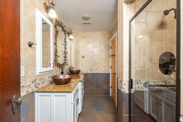 full bathroom featuring vanity, a textured ceiling, tile walls, visible vents, and tiled shower