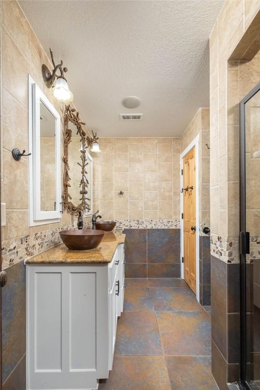 bathroom with visible vents, vanity, tile walls, a textured ceiling, and a stall shower