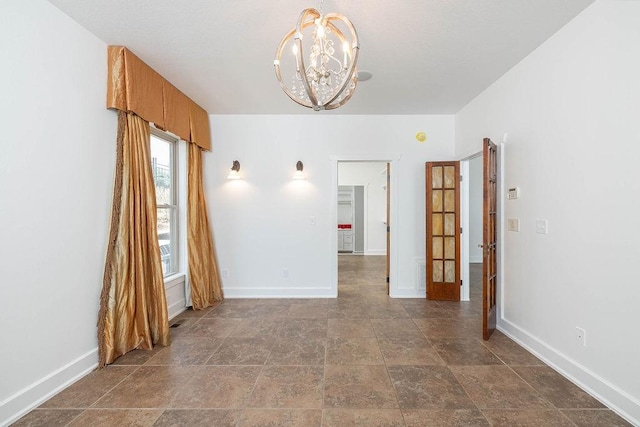 unfurnished room with an inviting chandelier, stone finish flooring, and baseboards