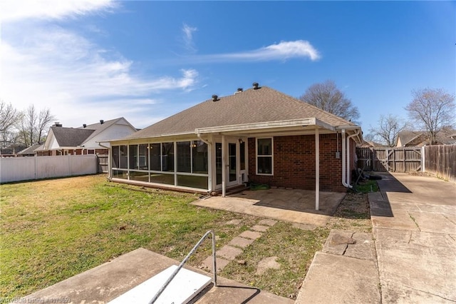 rear view of house featuring a fenced backyard, brick siding, a lawn, a sunroom, and a patio