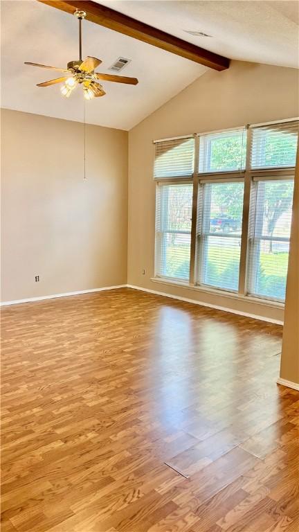 empty room featuring a healthy amount of sunlight, light wood finished floors, vaulted ceiling with beams, and visible vents