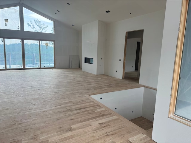 unfurnished living room featuring a glass covered fireplace, high vaulted ceiling, wood finished floors, and visible vents