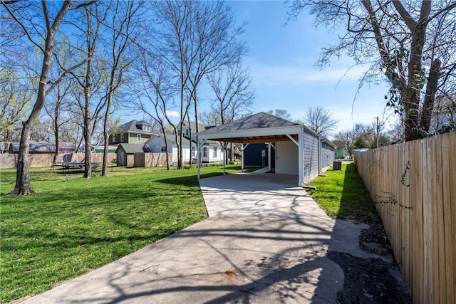 exterior space featuring an outdoor structure, concrete driveway, fence, a yard, and a storage shed