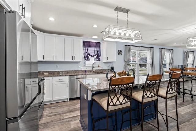kitchen featuring white cabinets, a kitchen island with sink, wood finished floors, stainless steel appliances, and a sink