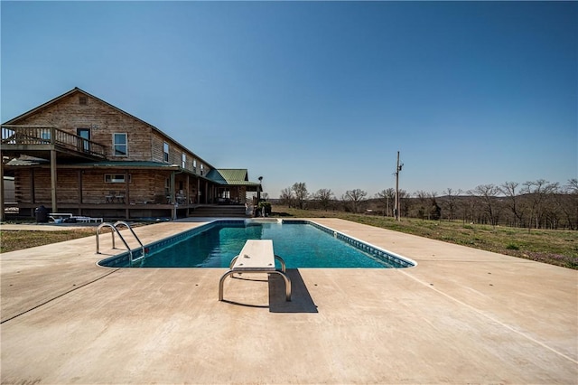 outdoor pool with a diving board, a deck, and a patio area
