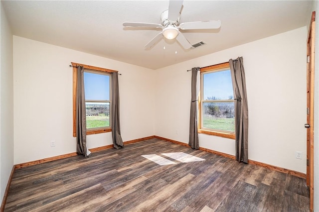 spare room featuring dark wood-type flooring, baseboards, and a healthy amount of sunlight
