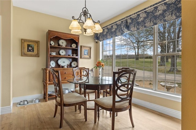 dining space featuring light wood-style flooring, a notable chandelier, and baseboards