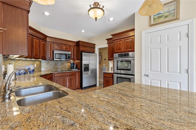 kitchen with recessed lighting, decorative backsplash, a sink, light stone countertops, and appliances with stainless steel finishes