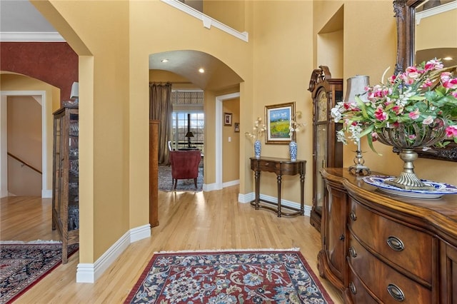 foyer entrance featuring a towering ceiling, arched walkways, baseboards, and light wood finished floors