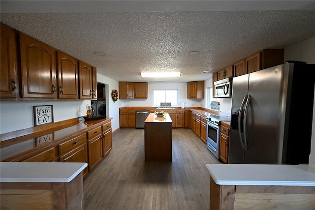 12766 Rocky Hill Rd, Prairie Grove, AR 72753 - kitchen featuring dark wood-type flooring, a textured ceiling, a kitchen island, appliances with stainless steel finishes, and brown cabinets